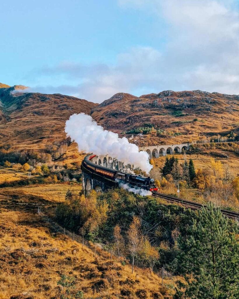 Steam train crossing a bridge with golden coloured hills