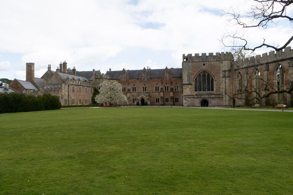 A large grassy lawn with an old stone building partially in ruins, built in red stone with large windows like a church