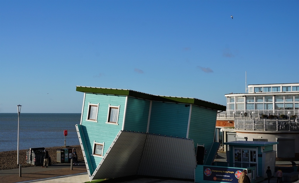An upside down turquoise house on the shore of a big body of water