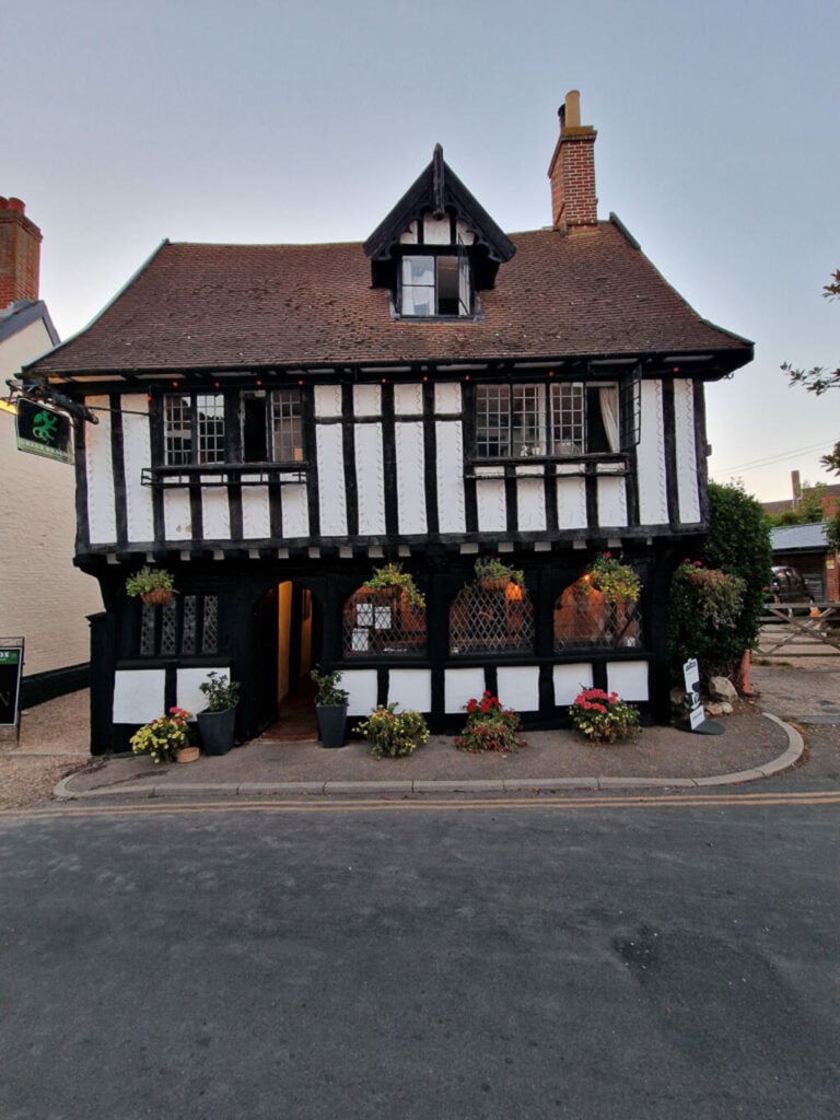 An old white timber framed building on the side of a road with flower baskets hanging outside